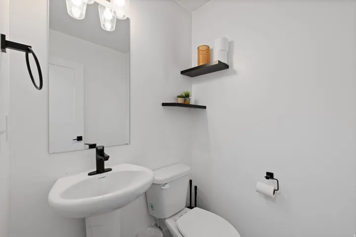 Pedestal sink with a matte black faucet, wall-mounted mirror, and black accent shelving