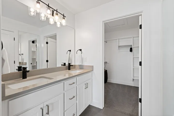 Dual vanity with light-toned countertop and integrated sinks, matte black fixtures, and a multi-bulb vanity light