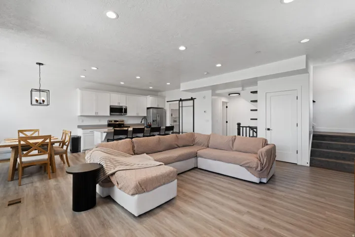 Open-concept living area featuring wood-finish flooring, recessed lighting, a modern kitchen with white cabinetry, and a dining area with a contemporary chandelier