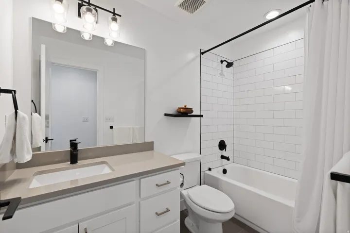 Bathroom featuring a vanity with an integrated sink, a large mirror, and a bathtub with subway tile surround and black fixtures