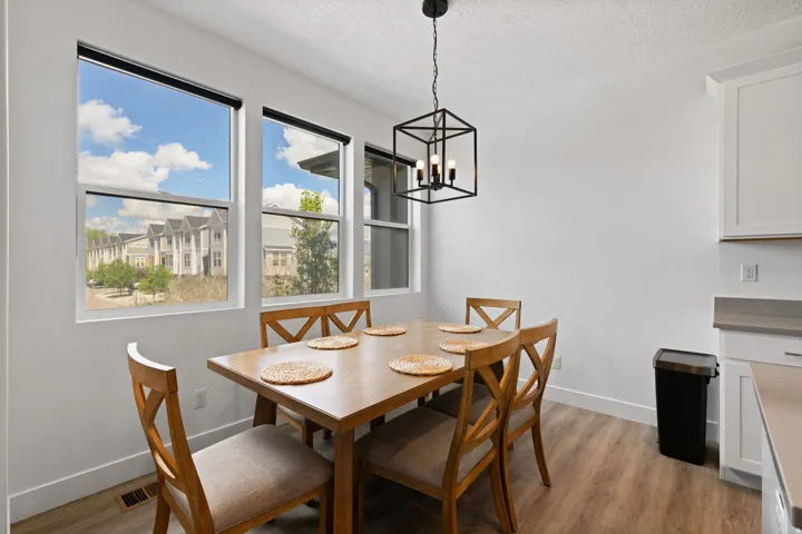 White walls, wood-finish flooring, multiple windows, black open-frame chandelier, and white cabinetry