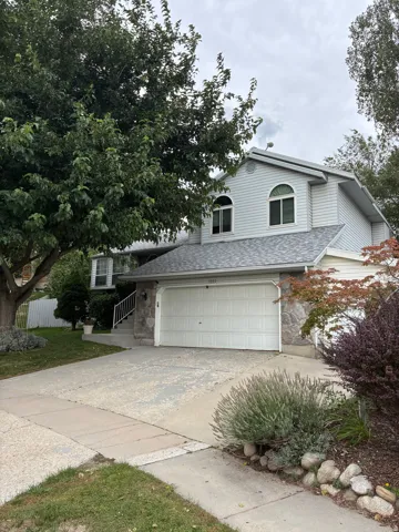 Two-story residence featuring siding and stone facade, arched upper-level windows, attached two-car garage, concrete driveway, and established landscaping