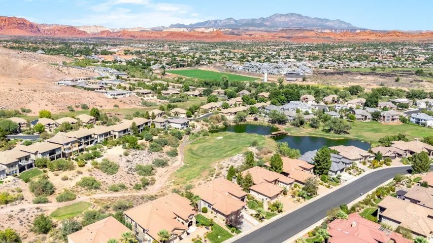 Aerial perspective showcasing a residential community with red rock mountain scenery, a golf course, and a pond feature