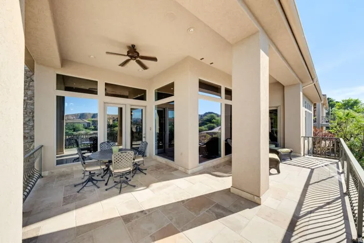 Expansive covered patio featuring a ceiling fan, stone tile flooring, and a decorative metal railing