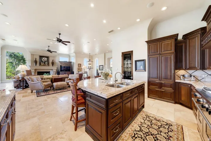 Gourmet kitchen with wood cabinetry and stone countertops, stainless steel appliances, and a central island with dual sinks