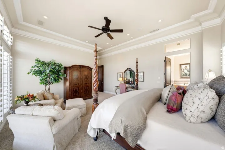 Tray ceiling with crown molding, recessed lighting, ceiling fan, plantation shutters, and wood-paneled door