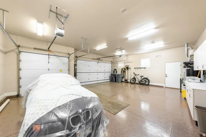 Three-car garage with epoxy flooring, two overhead garage doors, integrated lighting, and built-in white cabinetry
