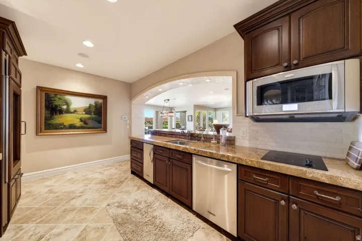 Kitchen featuring an arched pass-through, stainless steel appliances, dark wood cabinetry, and a stone countertop