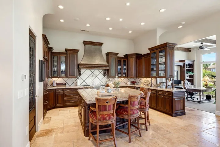 Expansive kitchen featuring wood cabinetry, a large central island with seating, a decorative range hood, and tile flooring