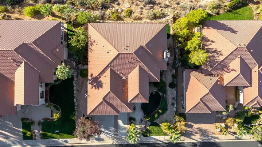 Terracotta tile roof, attached garage, paved driveway, mature landscaping, and an organized lot