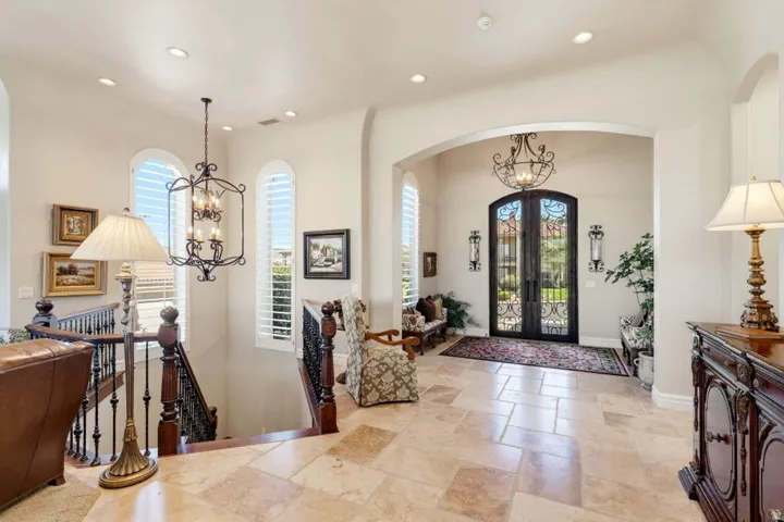 Arched entryway with double doors featuring decorative ironwork, complemented by light-toned tile flooring, recessed lighting, and a dark wood staircase with ornate iron balusters