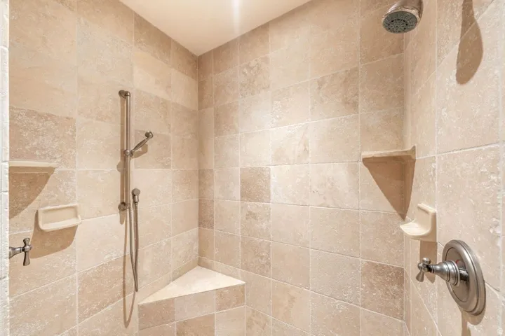 Tiled shower enclosure featuring a corner bench, handheld shower sprayer, and a fixed shower head