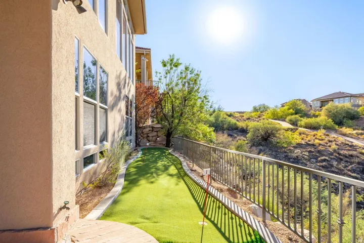 Exterior stucco finish, multiple large windows, artificial turf putting green, metal railing, and natural landscape
