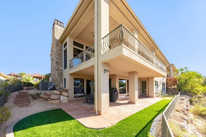 Multi-level stucco exterior with a stone chimney, upper-level balcony with decorative railings, and a ground-level covered patio