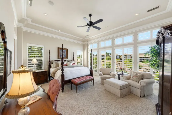 Tray ceiling with recessed lighting, crown molding, wall of windows with plantation shutters, ceiling fan, and carpeted flooring