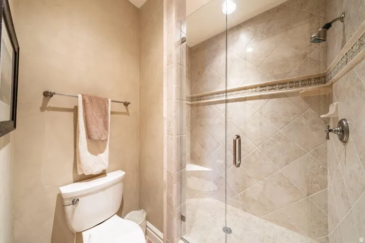 Glass-enclosed shower with ceramic tile walls, decorative tile band, built-in shower bench, and a rain showerhead