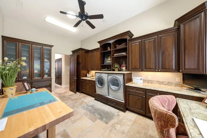 Warm wood-finish cabinetry, light-toned stone tile flooring, built-in display hutch, stone-look countertops, and recessed lighting