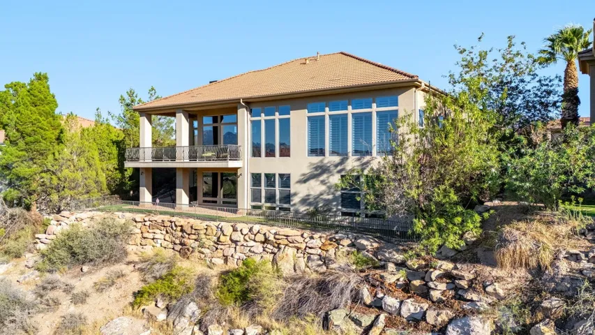 Stucco exterior with a tile roof, featuring an upper-level covered balcony with a metal railing, and extensive window placements
