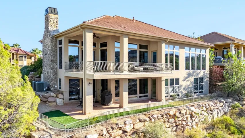Multi-level exterior featuring a stone chimney, extensive window placement, upper-level balcony, lower-level patio, and a terraced landscape