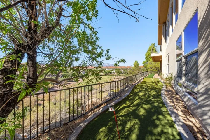 Stucco exterior with multiple windows, wrought iron railing, artificial turf putting green, and a distant golf course