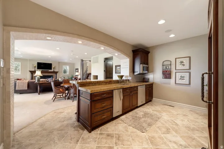Wet bar featuring wood cabinetry, integrated appliances, and a stone-finish countertop