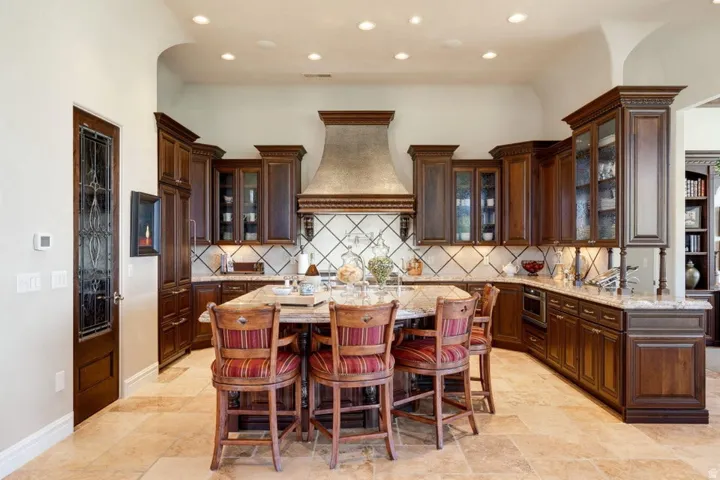 Spacious kitchen featuring rich wood cabinetry, stone countertops, a large center island, and patterned tile backsplash