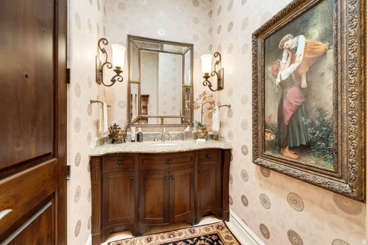 Ornate vanity with integrated sink, stone countertop, decorative sconce lighting, and a framed mirror