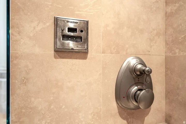 Tiled shower surround with a brushed metal steam shower control panel and a brushed metal shower valve