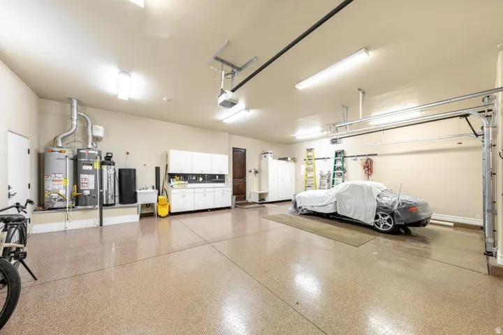 Spacious garage with an epoxy floor, built-in cabinetry, utility sink, and multiple water heaters