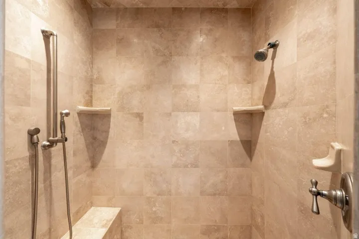 Tiled shower enclosure featuring a built-in bench, two corner shelves, a handheld showerhead, and a fixed showerhead