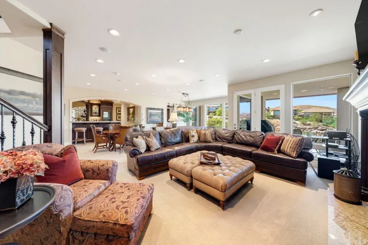 Recessed lighting, built-in bar with seating, light-colored carpeting, French doors to exterior, and fireplace with stone surround