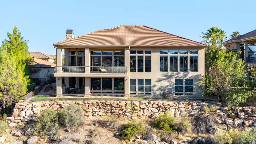 Two-story stucco exterior with a tile roof, an upper-level balcony, a lower-level patio, and extensive window placements