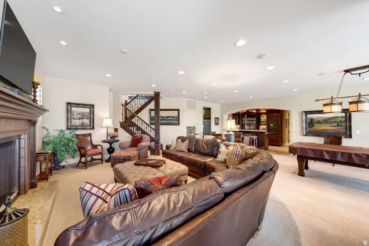 Spacious lower level featuring a built-in wet bar with cabinetry, recessed lighting, a fireplace with a wood mantel, and a prominent staircase with dark wood railings