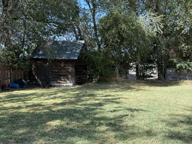 Expansive backyard featuring a wood-sided shed with a metal roof, mature trees, and a wooden fence