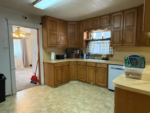 Kitchen featuring wood cabinetry, laminate countertops, a single basin sink, and a built-in dishwasher