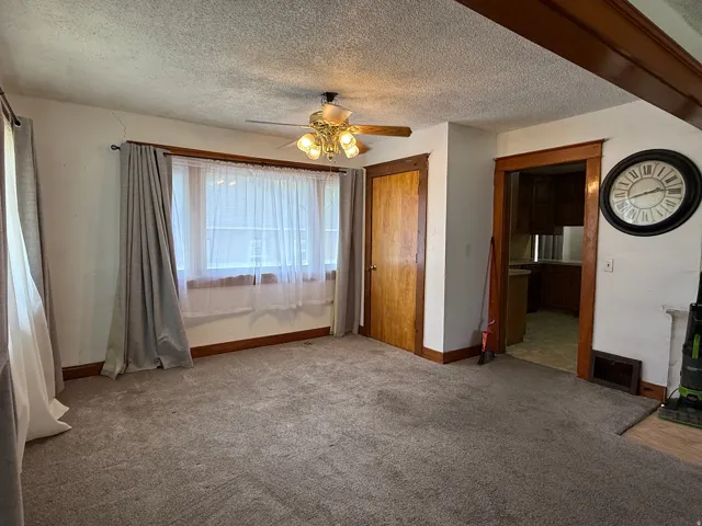 Textured ceiling, ceiling fan with light fixture, carpeted flooring, wood trim, and wood-finish door