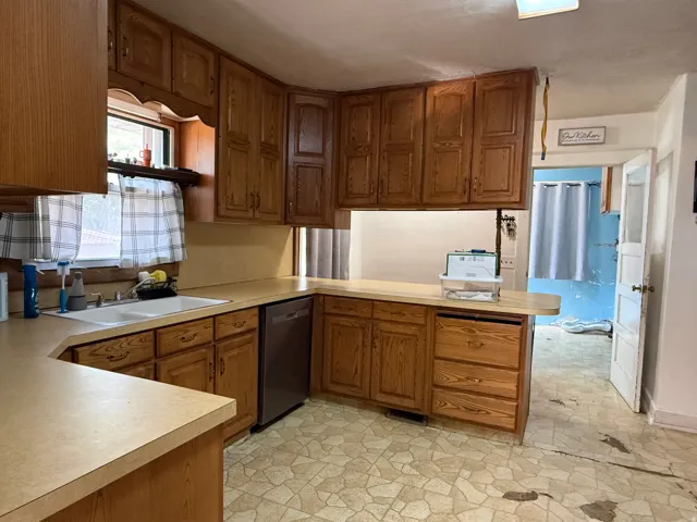 Wood cabinetry, double basin sink, stainless steel dishwasher, light-toned countertops, and patterned floor tiling