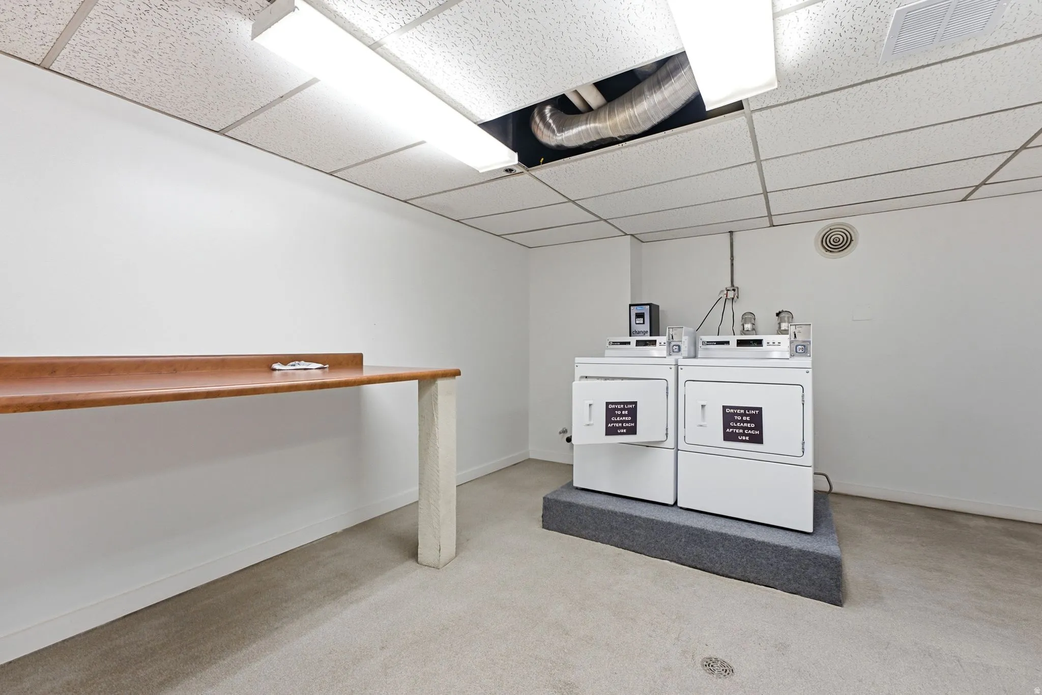 Laundry area featuring two white washing machines, a matching dryer, and a long wood-finish countertop