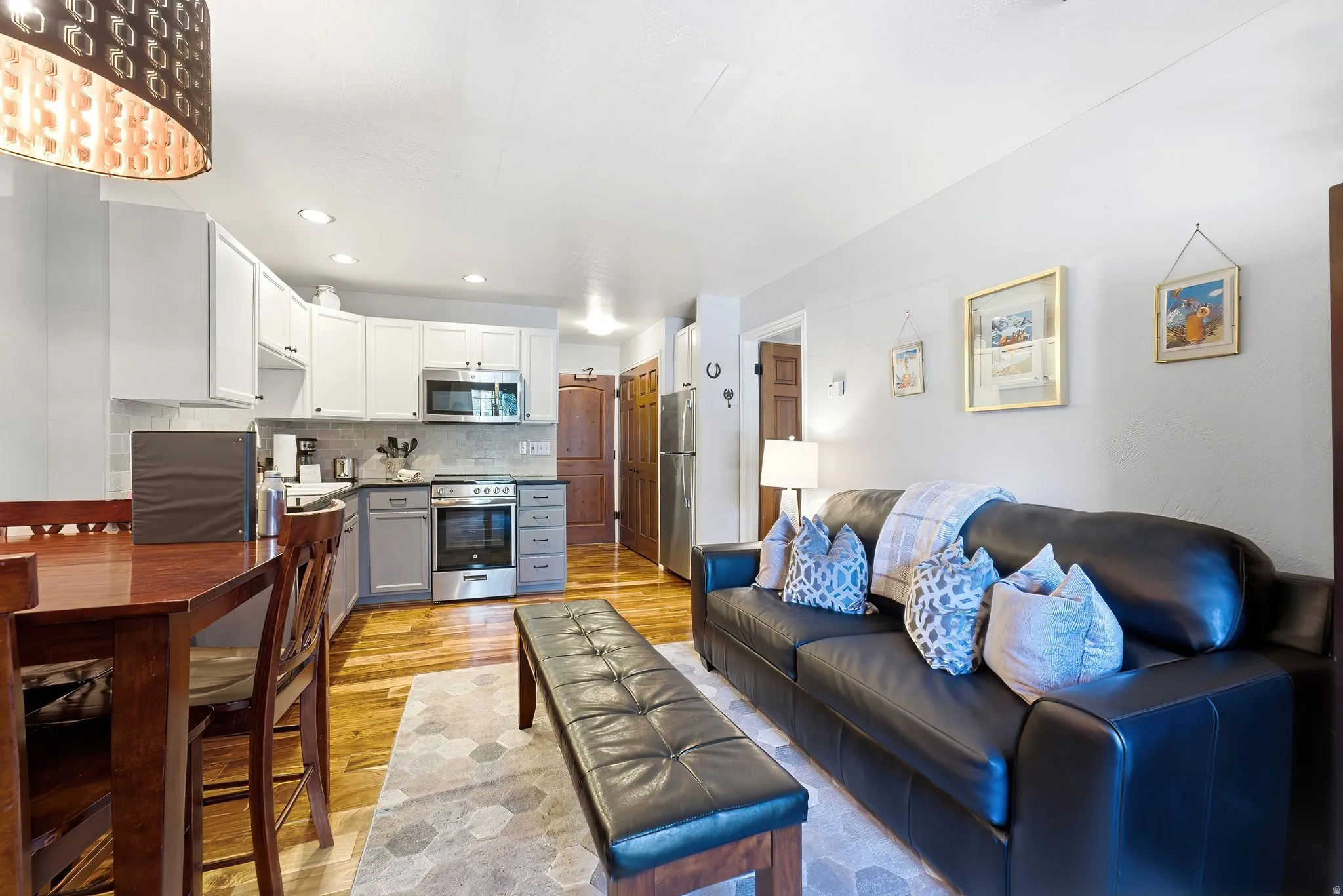 Open concept living area featuring wood-finish flooring, recessed lighting, and a kitchen with white upper and gray lower cabinetry, a tiled backsplash, and stainless steel appliances