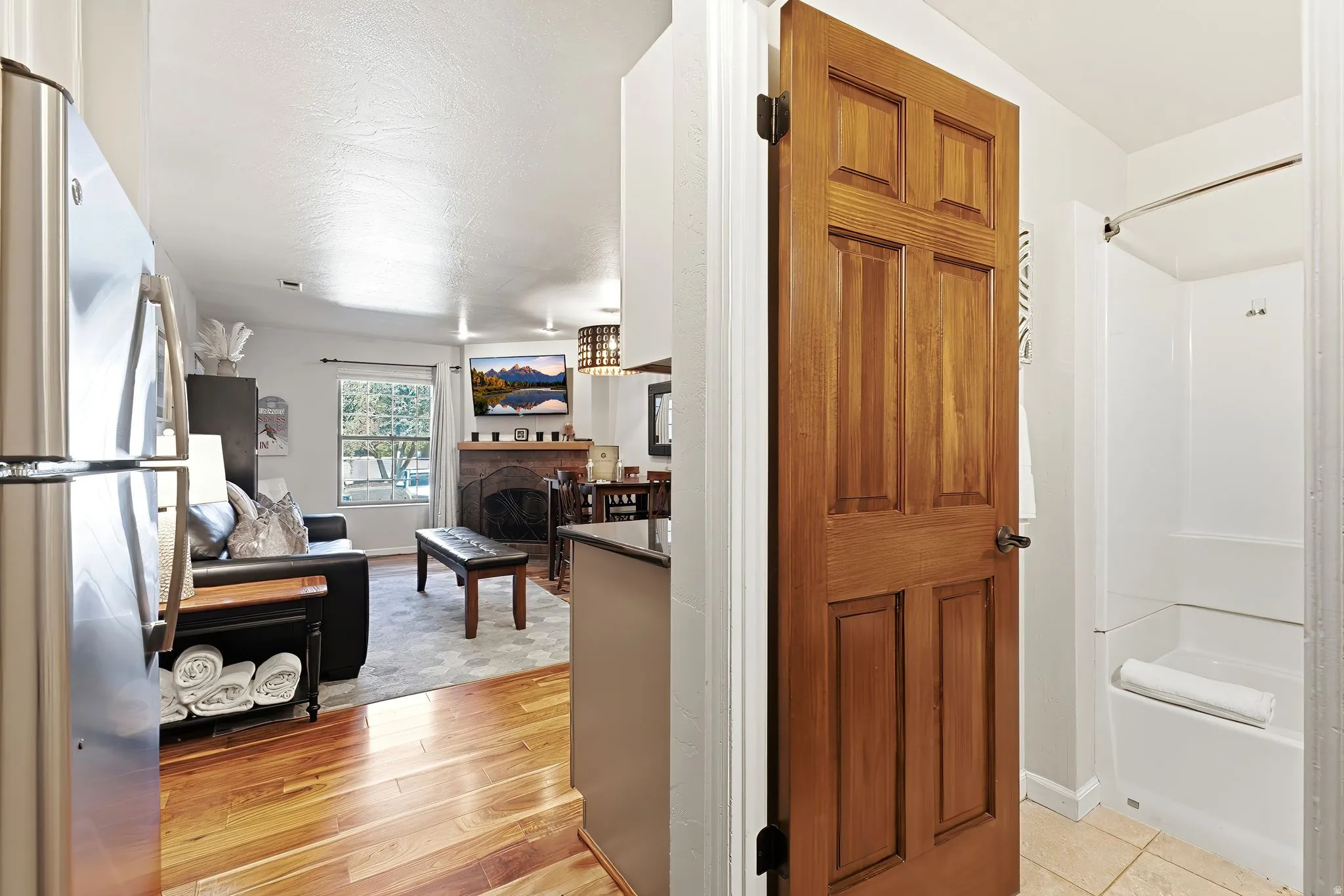 Hardwood flooring, stainless steel refrigerator, stone-front fireplace, paned window, and a paneled interior door