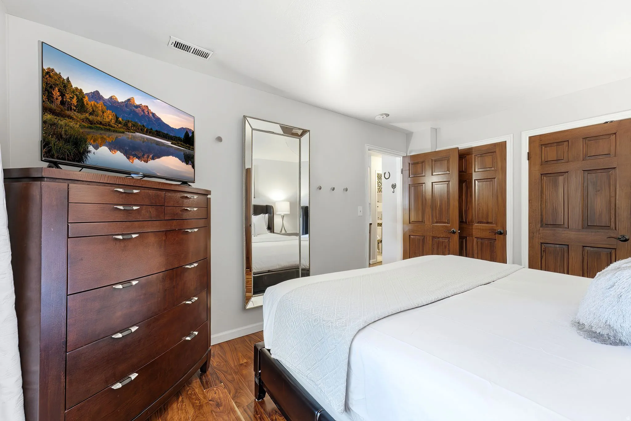 Spacious primary bedroom featuring hardwood flooring, recessed ceiling lighting, and a wood-finish dresser with chrome hardware