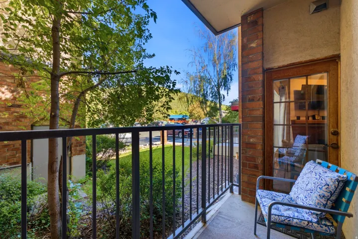 Private balcony with a brick-clad wall, wood-paneled door with glass inserts, and black metal railing