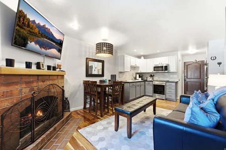Brick fireplace with a metal screen, wood-finish flooring, kitchen with stainless steel appliances, two-tone cabinetry, and a subway tile backsplash