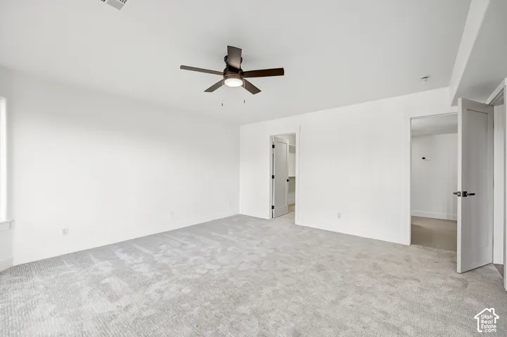 Expansive room featuring light gray carpeting, crisp white walls, a ceiling fan with integrated lighting, and multiple doorways