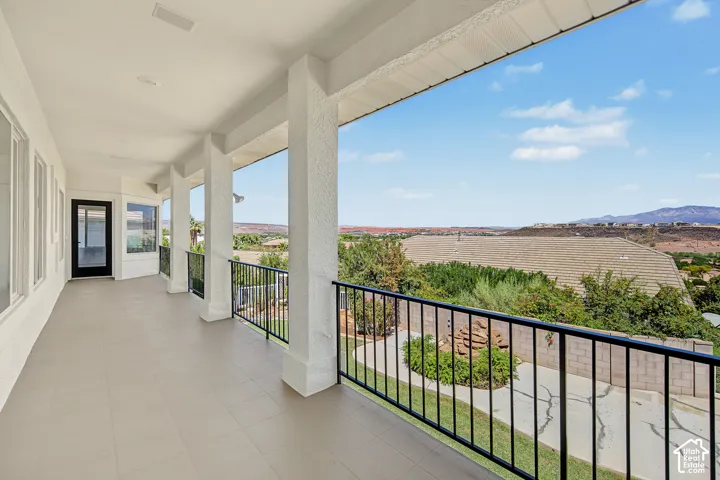 Expansive covered balcony featuring a black metal railing, light-toned flooring, multiple structural columns, and a glass-paned exterior door