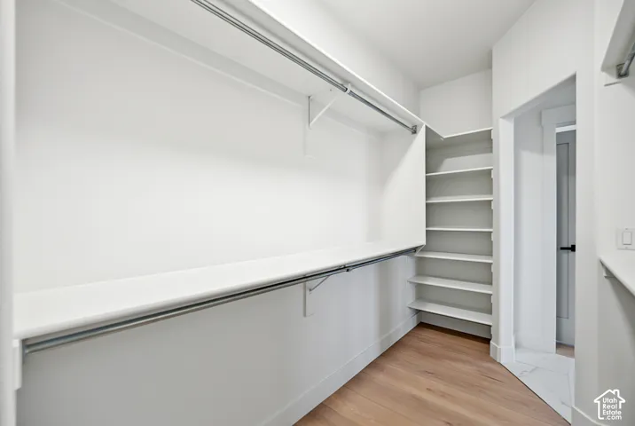 Dedicated closet space featuring wood-finish flooring, white walls, and built-in shelving