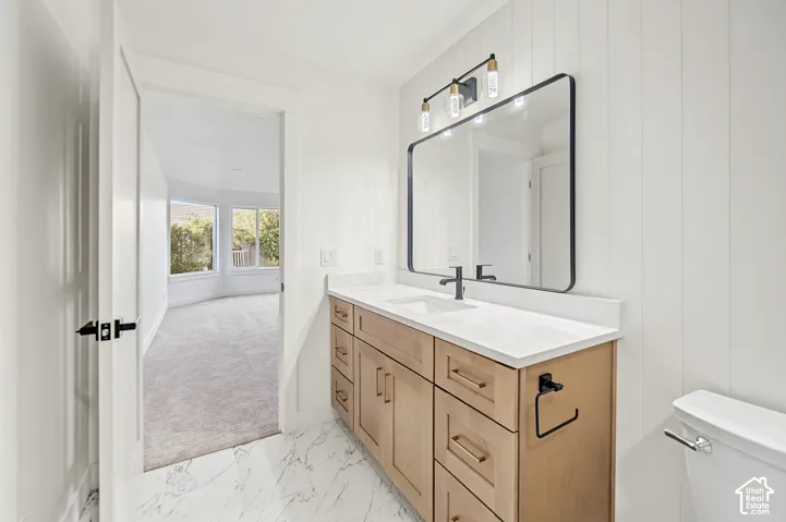 White marble-finish flooring, light wood vanity with multiple storage drawers, white countertop, black rectangular framed mirror, and vertical paneling accent wall
