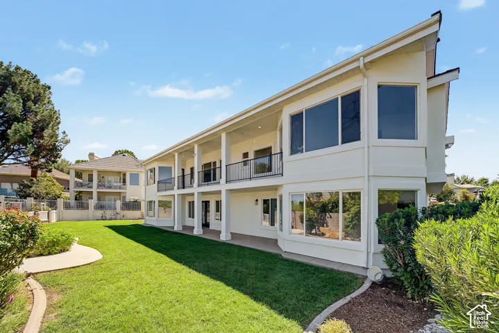 Exterior featuring a lower patio, upper balcony, multi-pane windows, and a landscaped lawn