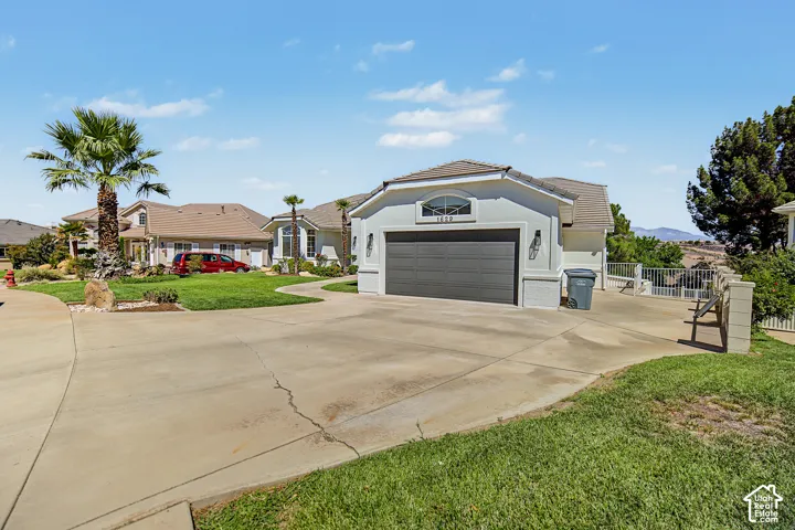 Stucco exterior with arched window detail, two-car garage, concrete driveway, and landscaped front yard with a palm tree