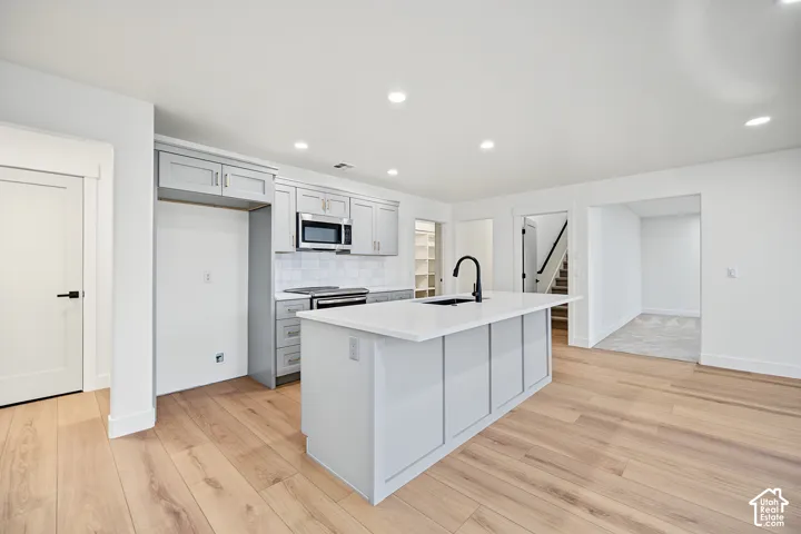 Kitchen featuring light gray cabinetry, white countertops, stainless steel appliances, and wood-finish flooring